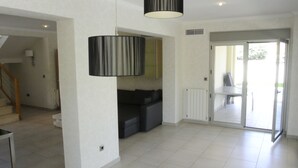 Un vaste espace de vie comprenant un escalier, un canapé noir, une table à manger et une porte-fenêtre coulissante donnant sur un espace extérieur.