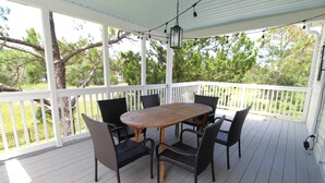 A covered outdoor patio with a wooden table and four chairs, surrounded by white railings and trees.
