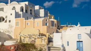 A coastal building with multiple balconies, a staircase leading to the upper levels, and a clear blue sky. - Sole d'oro Sunset & Caldera View Grand Suite (Santorini)