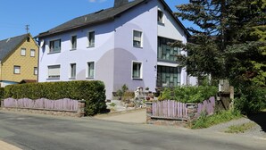 Ein zweistöckiges Haus mit hellvioletten Fassade, der Hausnummer 14 an der Vorderseite ist sichtbar, und ein verschlossener Auffahrt.
