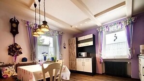 Ein gemütlicher Essbereich mit Holztisch und -stühlen, eine Küche mit Schränken und einer Mikrowelle sowie violette Vorhänge.
