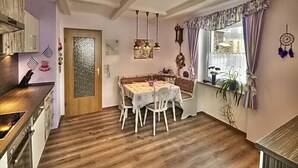Ein Essbereich mit Holzboden, einem Tisch mit Stühlen, einer Küchenzeile mit Schränken und einem Fenster mit Vorhängen.