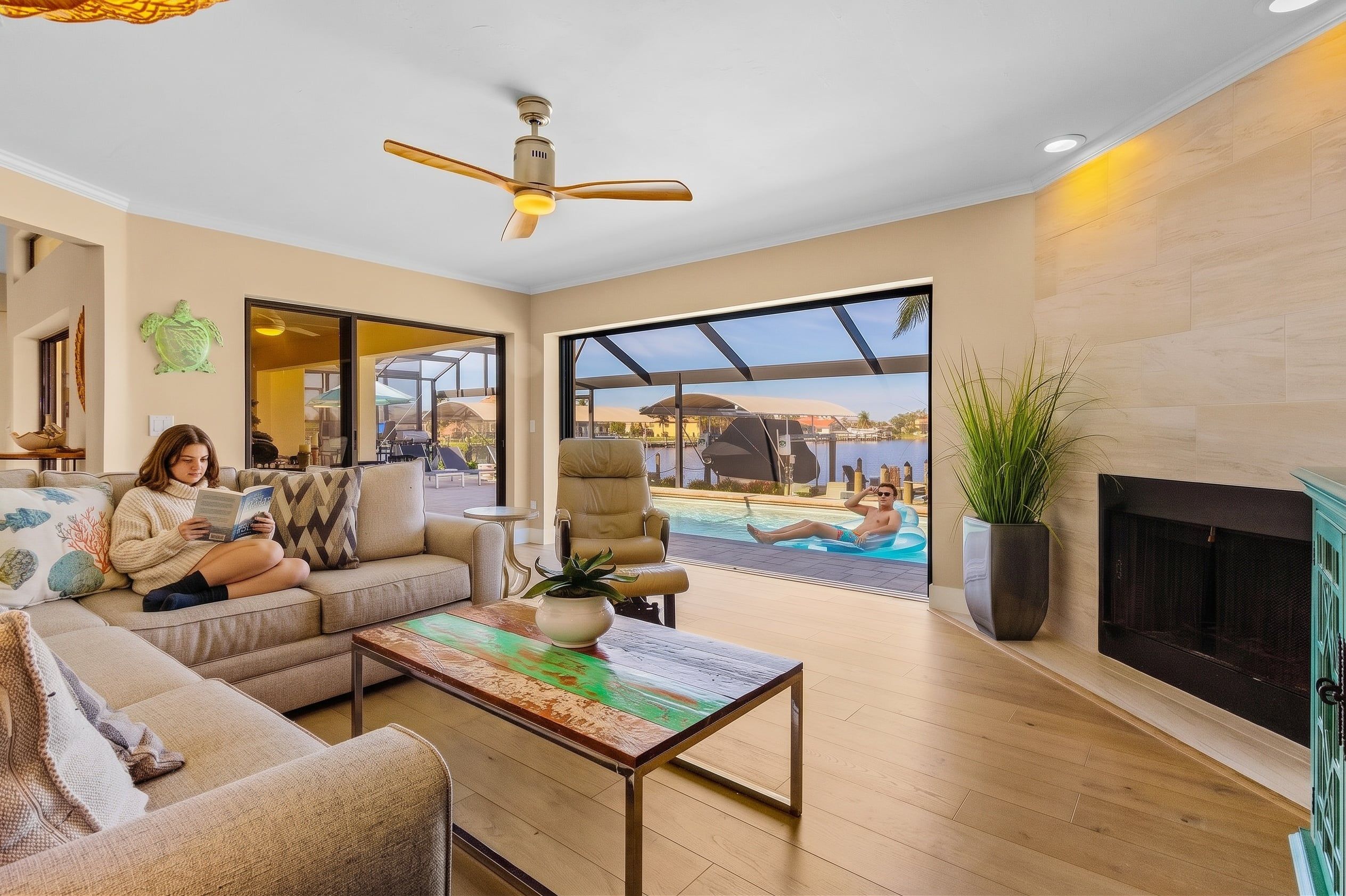 Amplia sala de estar con sofá, mesa de centro y chimenea. Un gran ventanal ofrece vistas a una piscina y un área de estar al aire libre.