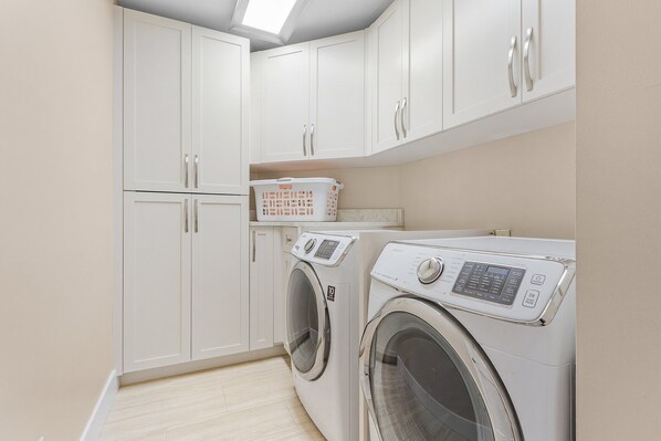 A laundry room with two front-loading washing machines, a drying rack, and white cabinets.