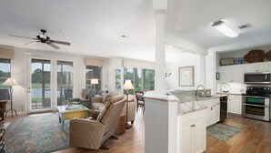 Un salon spacieux comprenant un canapé, une table basse et un ventilateur de plafond. Il y a également un coin cuisine équipé d’un four à micro-ondes, d’un four et de placards.