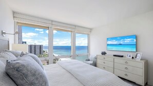 A bedroom with a large bed, a dresser, a TV, and a view of the ocean.