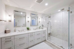 A modern bathroom with a large mirror, a glass shower enclosure, and a white vanity with multiple drawers. - La Mer at Park Shore (Naples)