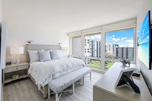 A bedroom with a bed, bedside tables, a bench, a desk, and a large window with a city view. - La Mer at Park Shore (Naples)