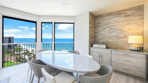 A balcony with a round table and wicker chairs, overlooking a beach and ocean.