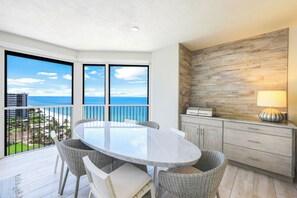 A balcony with a round table and wicker chairs, overlooking a beach and ocean.