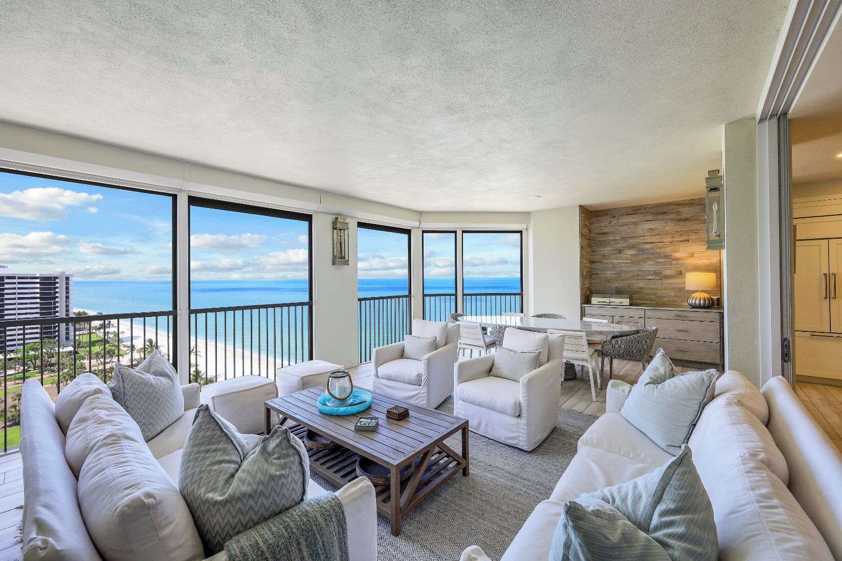 Un balcon avec vue sur l’océan, aménagé avec des canapés blancs et une table basse en bois.