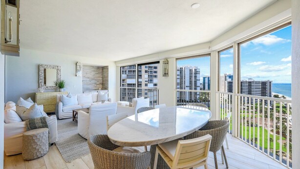A spacious balcony with a dining table and chairs, overlooking a cityscape and the ocean.