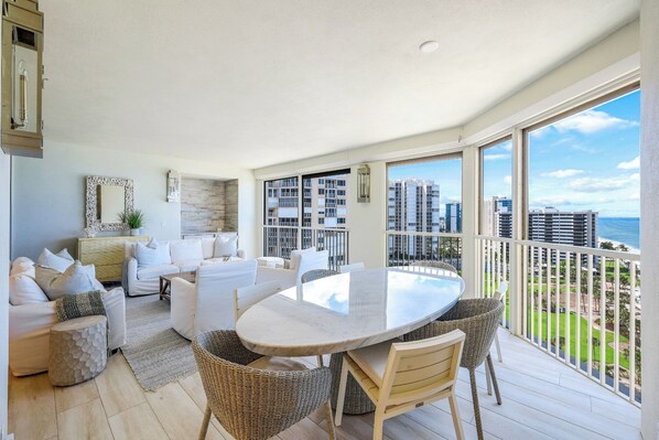 A spacious balcony with a dining table and chairs, overlooking a cityscape and the ocean.