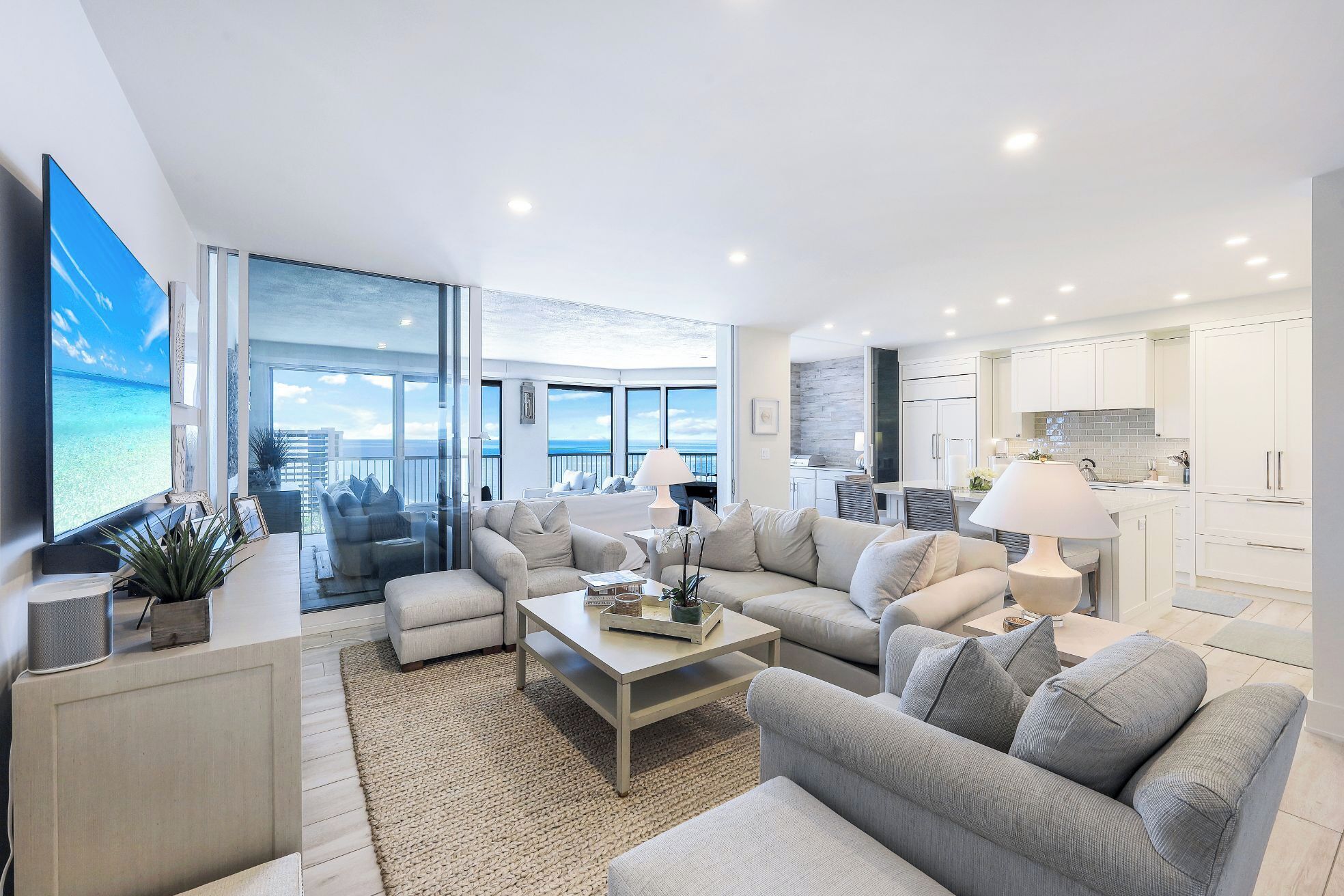 A spacious living room with a large flat-screen TV, comfortable seating, and a view of the ocean.