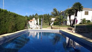 Una piscina con borde de azulejos, rodeada de un muro de piedra y follaje.
