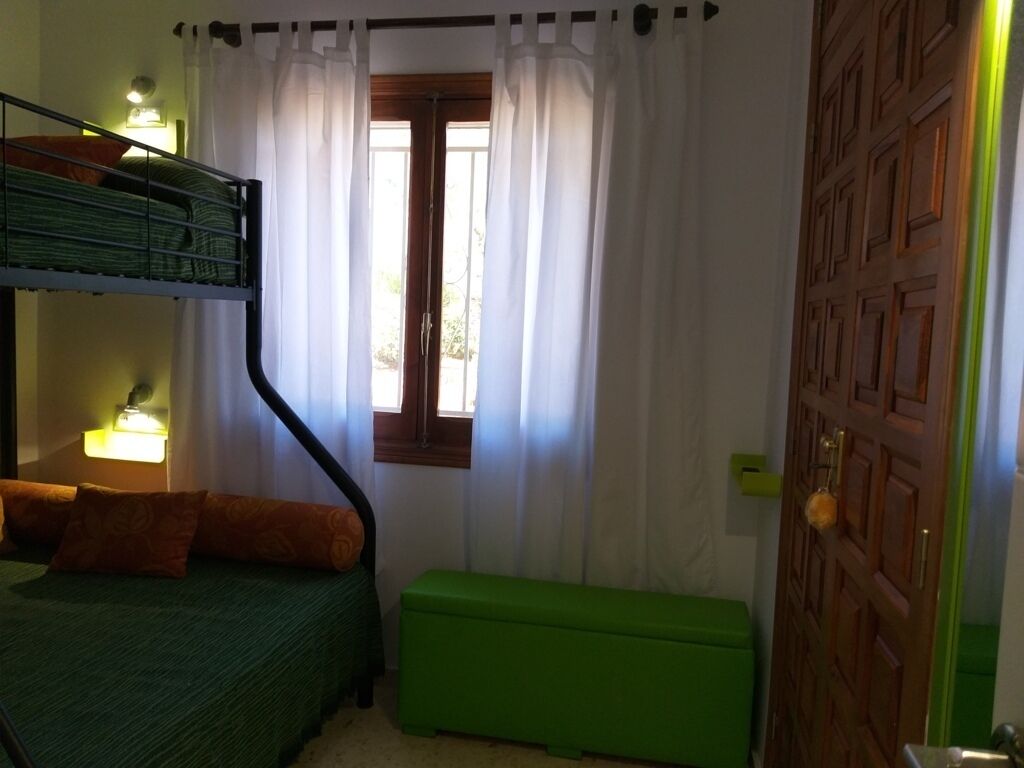 A room with bunk beds, a green bench, a window with curtains, and a wooden door.