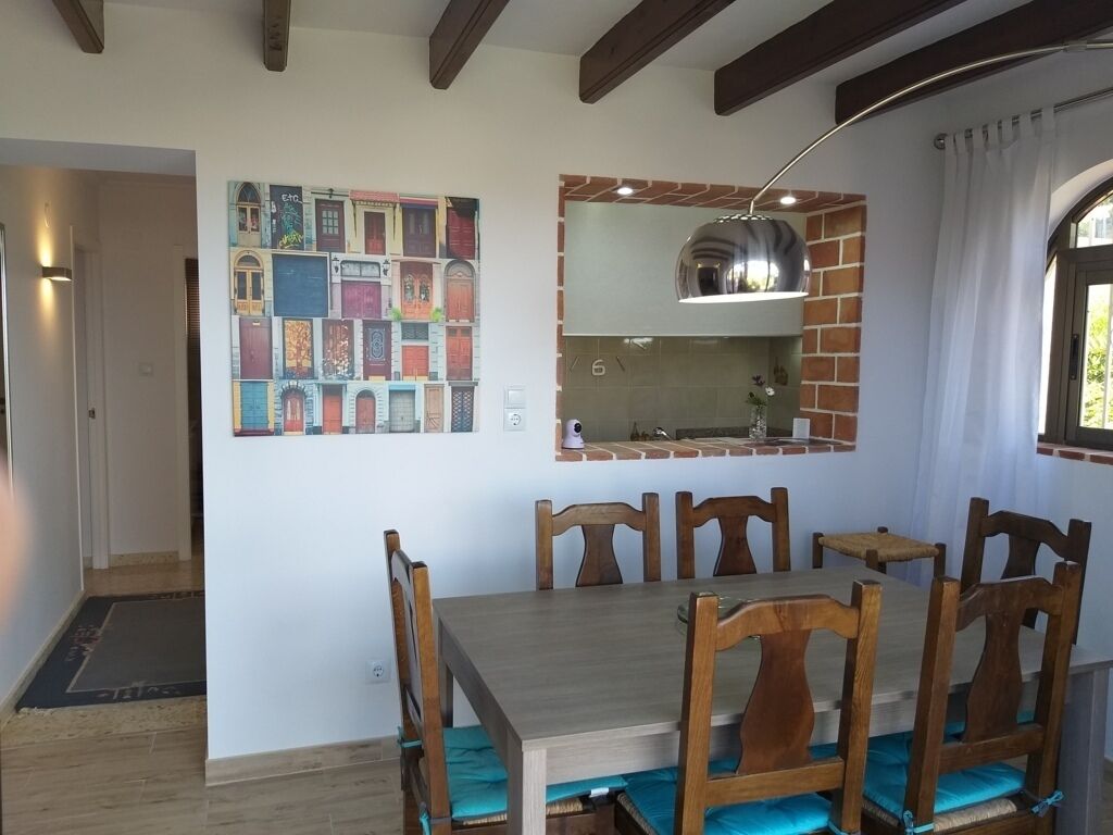 A dining area with a wooden table and chairs, a hanging light fixture, and a wall-mounted mirror above a brick backsplash.