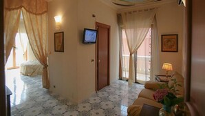 Une chambre d’hôtel équipée d’un lit, d’une télévision, d’un canapé et d’un balcon avec des rideaux.