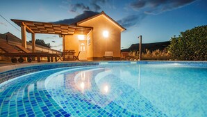 Una piscina con mosaicos azules, un pérgola de madera y un pequeño edificio con una luz en un lateral.
