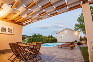 Une terrasse extérieure avec une piscine, des meubles en bois et une maison en arrière-plan.