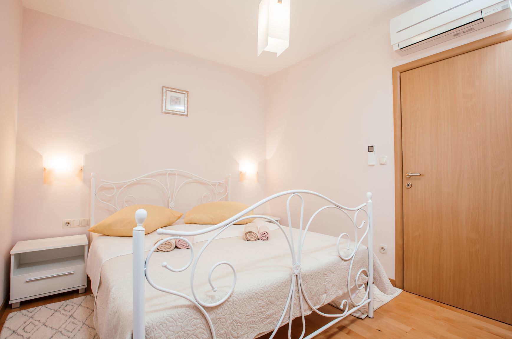 A bedroom with a white metal bed frame, two pillows, a bedside table, and a wooden door.