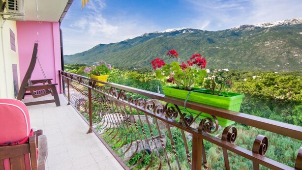 Uma varanda com vista para montanhas, uma parede rosa e plantas em vasos.