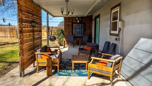 A covered patio area with wooden furniture, a grill, and a decorative door. - The Green Pony | Pet-friendly (Fredericksburg)