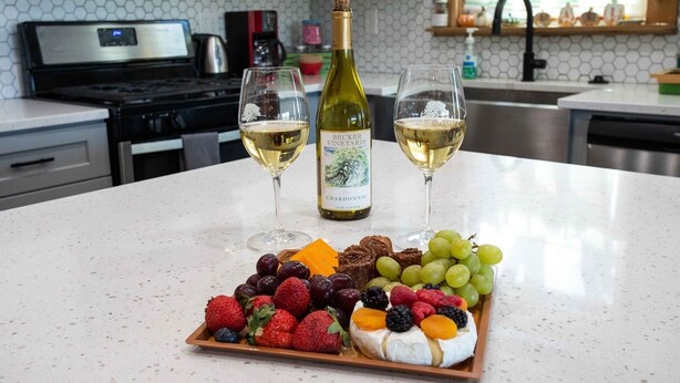 A kitchen counter with two glasses of white wine, a bottle of wine, and a fruit platter. - The Green Pony | Pet-friendly (Fredericksburg)