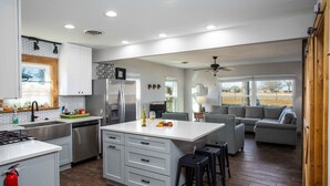 A modern kitchen with a central island, a dining area with a sofa, and a view of the outdoors. - The Green Pony | Pet-friendly (Fredericksburg)