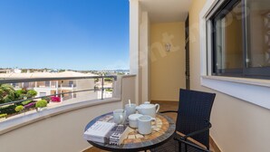 A balcony with a table set for tea, a chair, and a view of the cityscape.