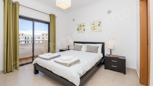 A bedroom with a bed, bedside tables, a window with curtains, and artwork on the wall.