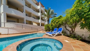 A swimming pool with a hot tub, lounge chairs, and a building with balconies.