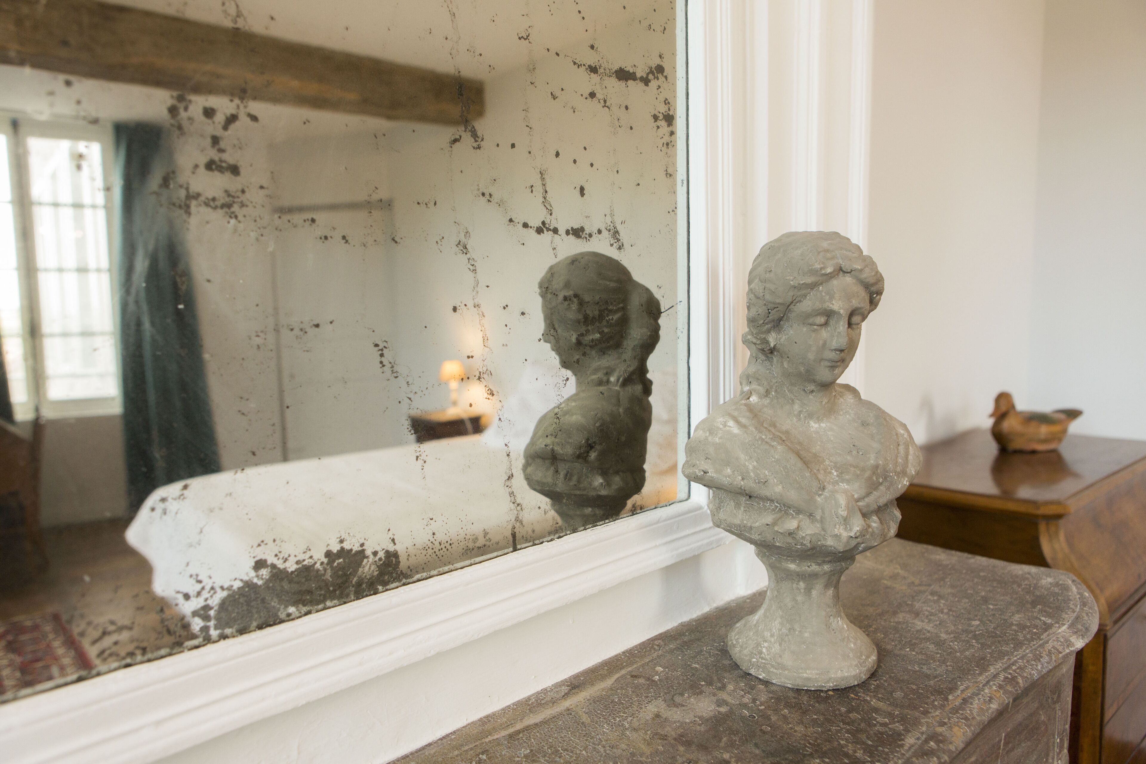 A room with a window reflecting a bust sculpture on a mantelpiece.