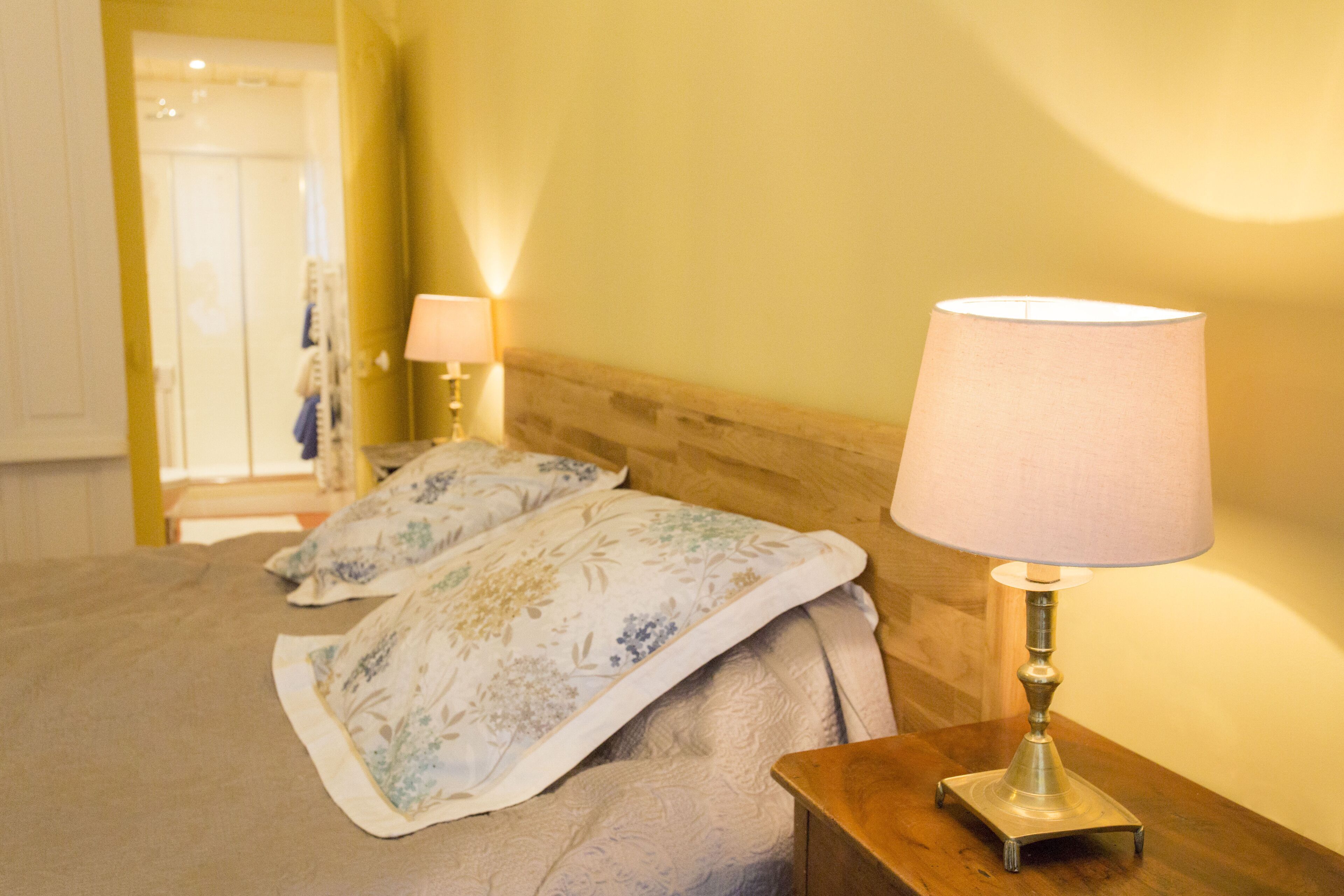 A neatly made bed with floral bedding, a bedside lamp, and a wooden nightstand.