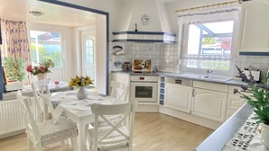 A modern kitchen with white cabinets, a built-in oven, and a window with a view of the outside. - Vacation apartment, ground floor, WLAN, covered terrace, wood-burning stove (Krummhörn)