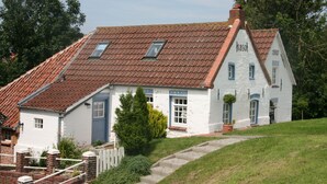 A traditional white house with a red-tiled roof, numbered 1851 and 1910, featuring a brick staircase and a white picket fence. - Vacation apartment, ground floor, WLAN, covered terrace, wood-burning stove (Krummhörn)