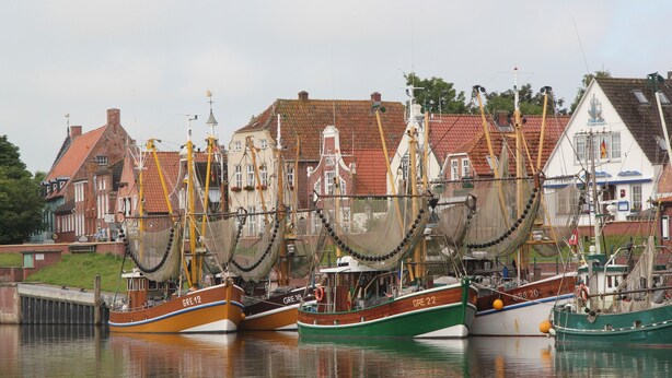 A harbor with several boats docked, surrounded by traditional buildings with red-tiled roofs. - Vacation apartment, ground floor, WLAN, covered terrace, wood-burning stove (Krummhörn)