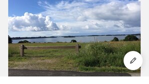 A bench in a grassy area with a lake and cloudy sky in the background. - House on the edge of the Gulf of Morbihan, the beach 2 minutes walk. (Baden)