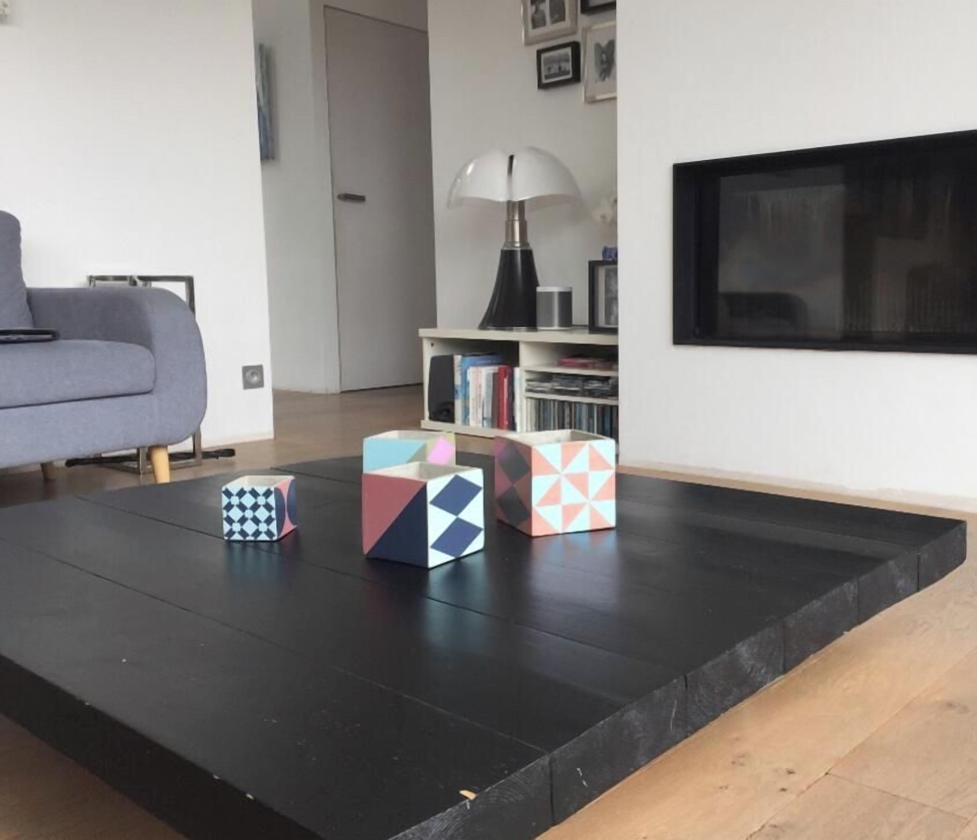 A living room with a sofa, a coffee table with geometric-patterned boxes, a bookshelf, and a mounted TV.
