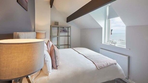 Une chambre à coucher avec un grand lit, une lampe de chevet, un radiateur et une fenêtre donnant sur la mer.