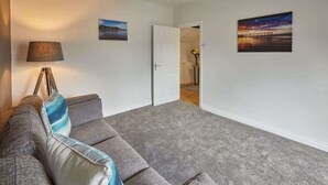 Un salon avec un canapé gris, une lampe et deux tableaux accrochés au mur.