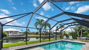A swimming pool with a metal roof structure, surrounded by a brick patio and palm trees. - Waterfront Piece of Paradise at Tiger Tail (Marco Island)