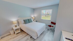 A bedroom with a bed, bedside lamps, a chair, a window, and a view of buildings outside.