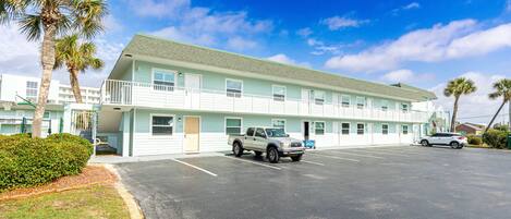 Un motel con aparcamiento, un edificio azul claro y palmeras.