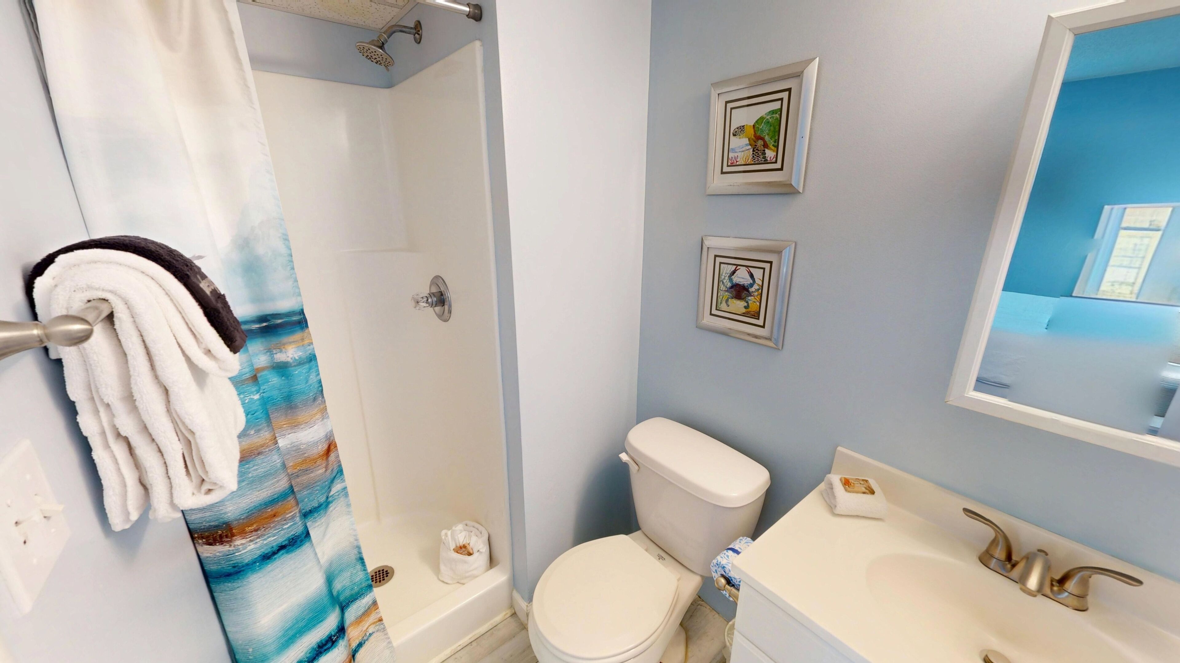 Un baño con ducha, inodoro, lavamanos y dos cuadros en la pared.