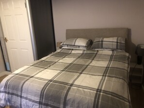 Uma cama com colcha xadrez, cabeceira e duas almofadas.