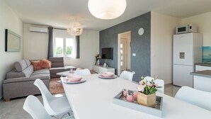 Una sala moderna con un sofá gris, una mesa de comedor blanca y una zona de cocina con refrigerador y microondas.