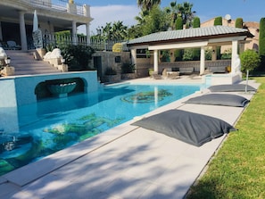 Piscina com fachada de pedra, cadeiras de descanso e área de estar coberta.