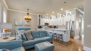 A modern kitchen with white cabinets, a stainless steel refrigerator, and a dining area with a blue sofa and a chandelier. - Blue Mountain on 30A - Rooftop Views - Pool - Steps to Beach! (Santa Rosa Beach)