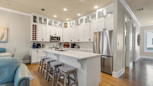 A modern kitchen with white cabinetry, a stainless steel refrigerator, and a central island with bar stools. - Blue Mountain on 30A - Rooftop Views - Pool - Steps to Beach! (Santa Rosa Beach)